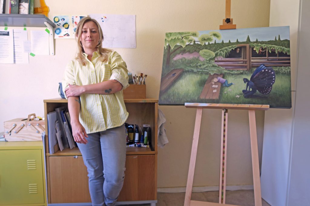 Laura Caseberry in home studio with easel, canvas, bushes and paints.